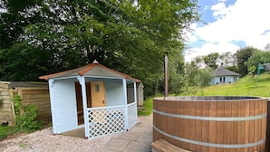 A small wooden cabin with a porch and a large wooden barrel. - Family Home With Large Garden and Pool Near Totnes (Totnes)
