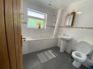 Et badeværelse med badekar, vask, toilet og et vindue med udsigt til et grønt felt.