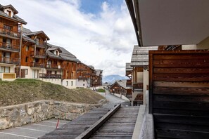 A row of wooden buildings with balconies, a stone retaining wall, and a wooden walkway leading to a parking area. - 200m from ski slopes, 1st floor, swimming pool, balcony, tv, ski locker, 23m², Les Orres (Les Orres)