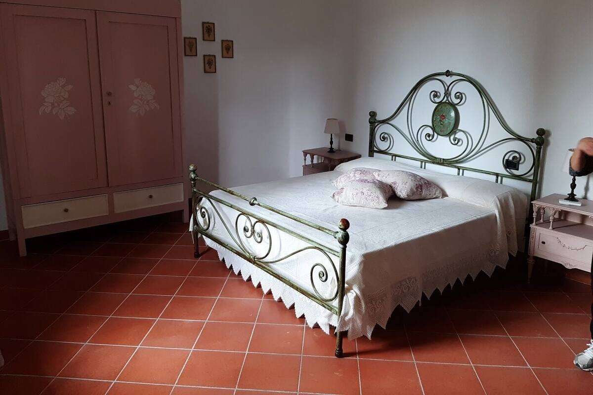 A bedroom with a metal bed frame, a pink wardrobe, and a tiled floor.