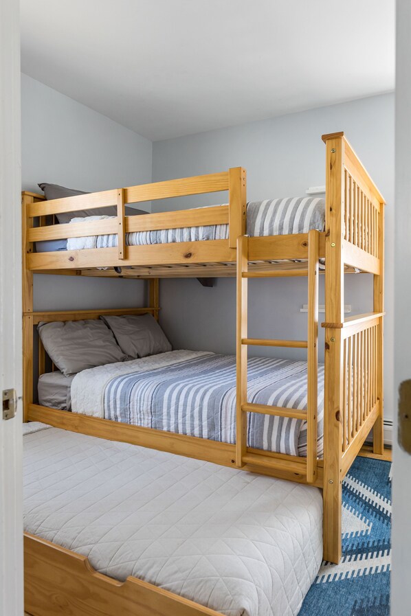 A bunk bed with a wooden frame, a lower bed with a quilted mattress, and a top bunk with pillows. - 4-minutes to Sugarbush, steps to Warren Village! (Warren)