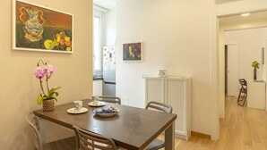Un comedor con mesa de madera, sillas, un florero con flores y dos cuadros en la pared.