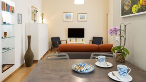 Una sala de estar moderna con un sofá, una mesa de comedor con platos y tazas, un televisor y una estantería.