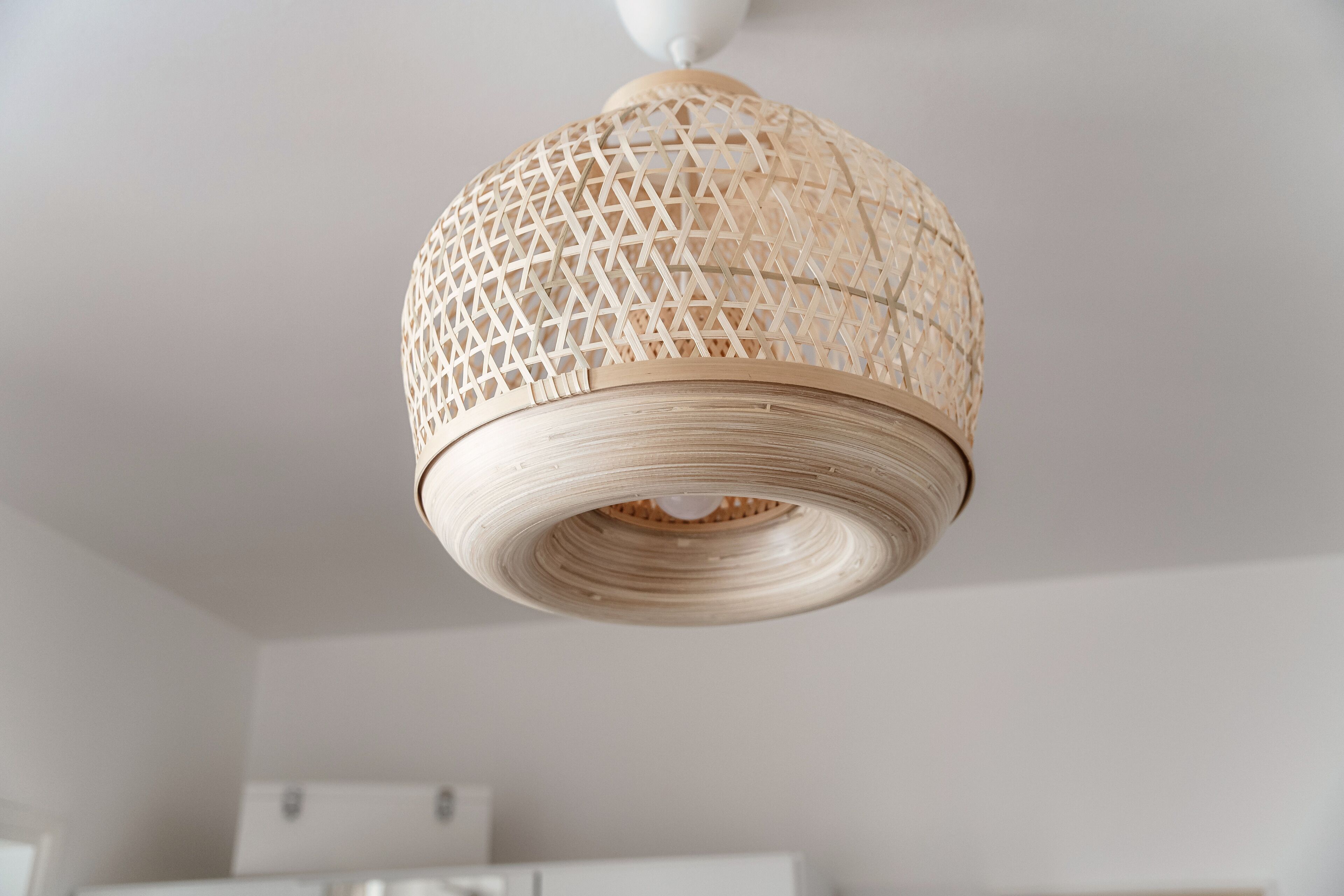 A woven, dome-shaped ceiling light fixture in a room with white walls and a white ceiling.