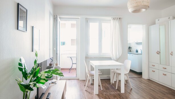 A bright, white room with a wooden floor, a white table with chairs, a potted plant, and a hanging light fixture. - Locarno City Apartments (Locarno)