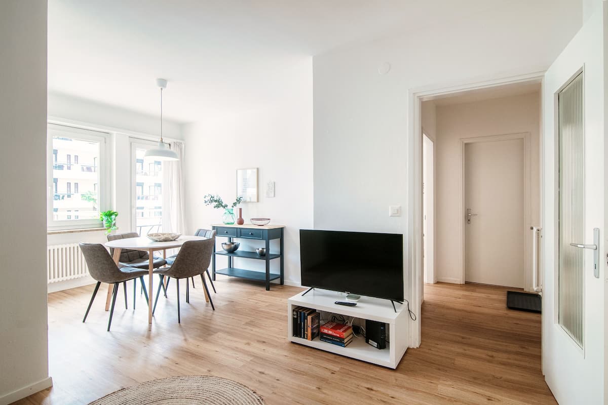 A modern living room with a dining area, a flat-screen TV, and a bookshelf.