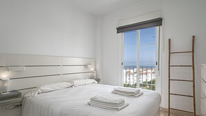Een moderne slaapkamer met een groot bed, een nachtkastje met lamp en uitzicht op gebouwen door een raam.