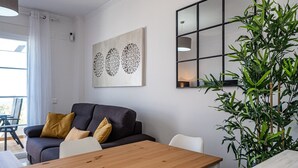 Een moderne woonkamer met een donkere bank, een houten eettafel en een grote spiegel aan de muur.