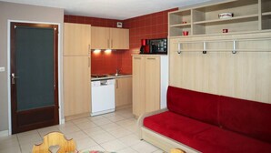 Cuina compacta amb rentavaixelles, un sofà vermell i armaris de fusta.