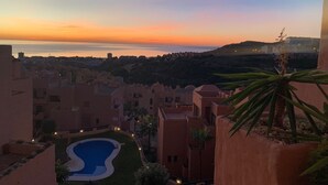 Une vue d’un paysage urbain côtier au crépuscule, avec une piscine, des immeubles à terrasses et une vue lointaine sur la mer.
