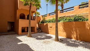 Une cour bordée de palmiers, un bâtiment orné d’arcades et un mur de pierre.