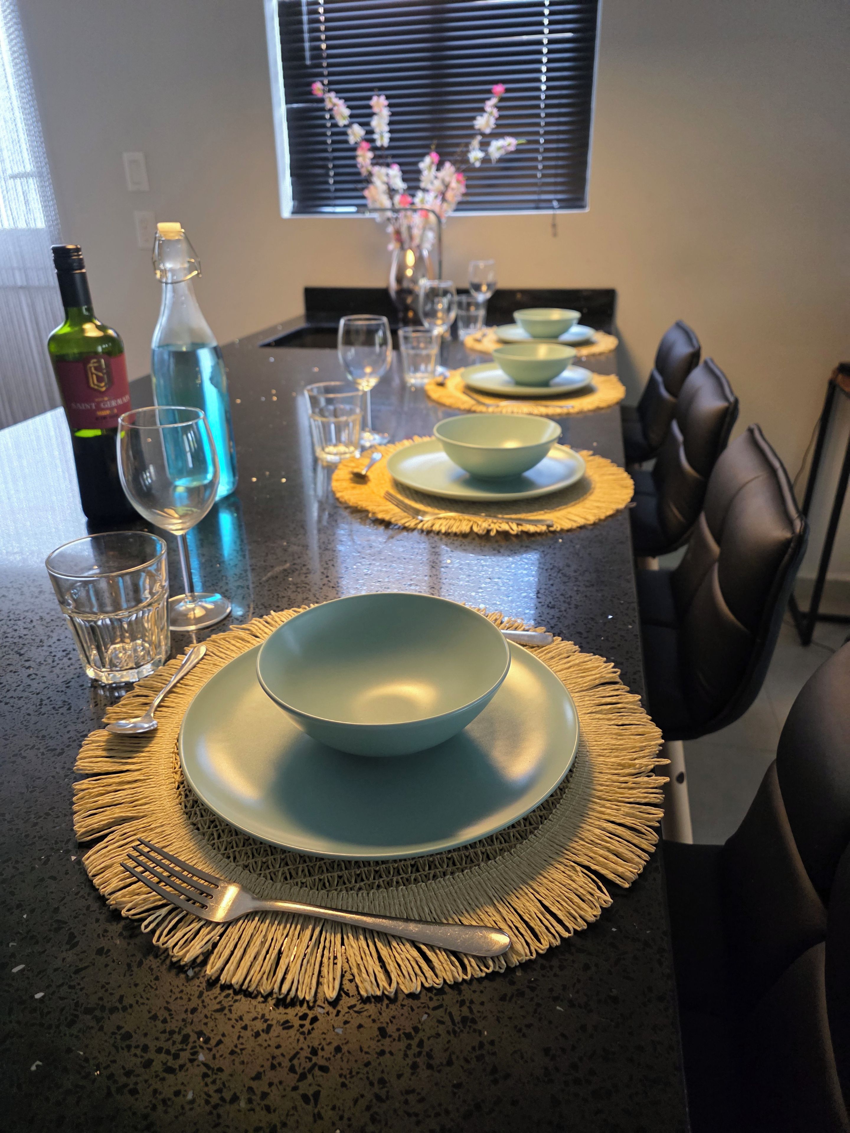A dining table set with plates, bowls, and cutlery, a bottle of wine, and a vase with flowers.