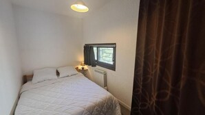 Et lille værelse med enkeltseng, et vindue, en radiator og en sengebordlampe.