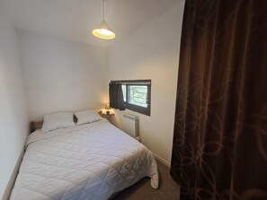 Una camera piccola con un letto singolo, una finestra, un termosifone e una lampada da comodino.