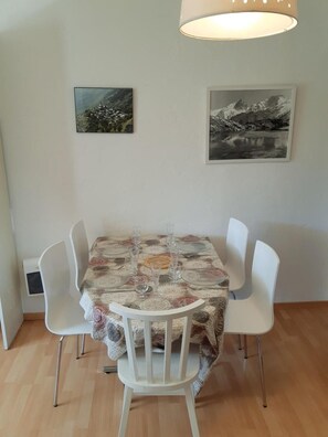 Un coin repas avec une table dressée pour quatre personnes, entourée de chaises blanches. Deux tableaux encadrés sont accrochés au mur, au-dessus de la table.