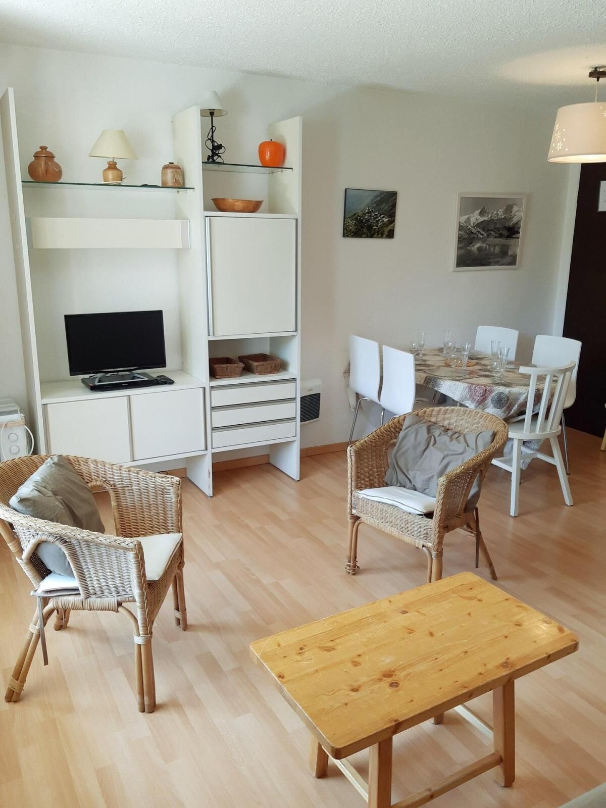 Een moderne woonkamer met een televisie, rieten stoelen, een houten tafel en een eethoek met stoelen en een tafel.