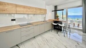 Eine moderne Küche mit Holzarbeitsplatte, Marmorfliesenspiegel und Meerblick durch große Fenster.