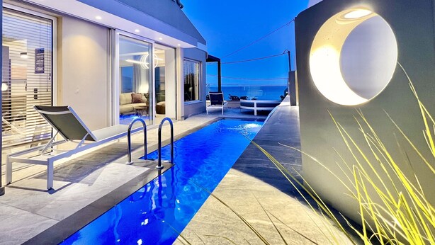 Ein moderner Poolbereich im Freien mit blauem Himmel, einer Lounge mit Sitzgelegenheiten und einer großen, beleuchteten Wandgestaltung.