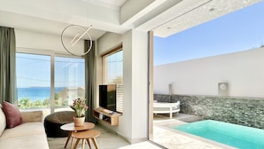 Ein modernes Wohnzimmer mit großem Fenster, einer Couch, einem kleinen Tisch und Blick auf einen Swimmingpool.
