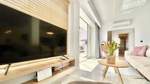 Ein modernes Wohnzimmer mit einem großen Flachbildfernseher, einer Holz-Unterhaltungseinheit, einem runden Couchtisch mit einem gewobenen Korb, einem beige farbenen Sofa und einer Glastür zu einem Außenbereich.