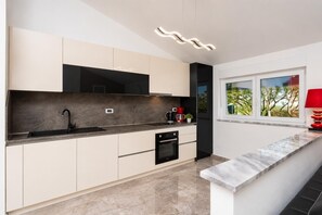 Eine moderne Küche mit Backofen, Kaffeemaschine und einem Fenster mit Blick auf Bäume.