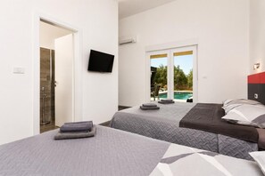 Habitación de hotel con dos camas, televisor, vista a la piscina y puerta que da a un baño.