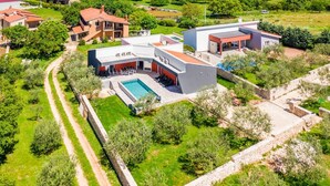 Een modern huis met een zwembad, omringd door weelderige begroeiing en een stenen muur.