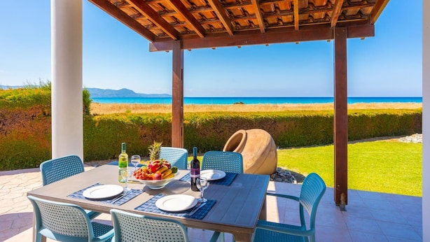 A covered outdoor dining area with a table set for two, overlooking a beach with clear blue waters and distant mountains. - Blue Bay Villa Thea - Three Bedroom Villa, Sleeps 6 (Polis)
