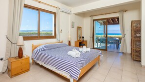 A bedroom with a bed, bedside table, lamp, and a view of the sea through a sliding glass door. - Blue Bay Villa Thea - Three Bedroom Villa, Sleeps 6 (Polis)