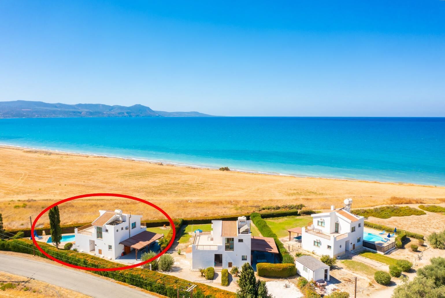 A coastal property with two white houses, a swimming pool, and a view of the sea.