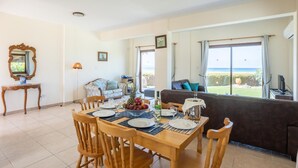 A dining area with a table set for four, a sofa, and a view of the sea. - Blue Bay Villa Thea - Three Bedroom Villa, Sleeps 6 (Polis)