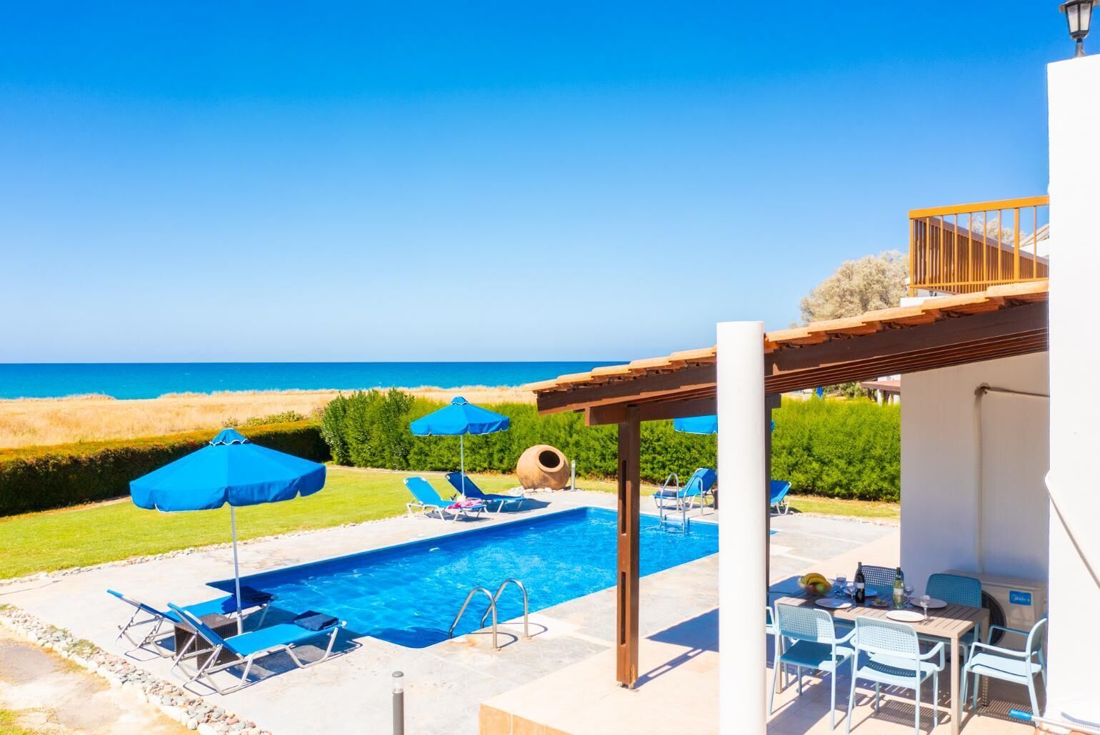 Ein Poolbereich mit Liegestühlen und Sonnenschirmen, einer Pergola und Blick auf den Strand.
