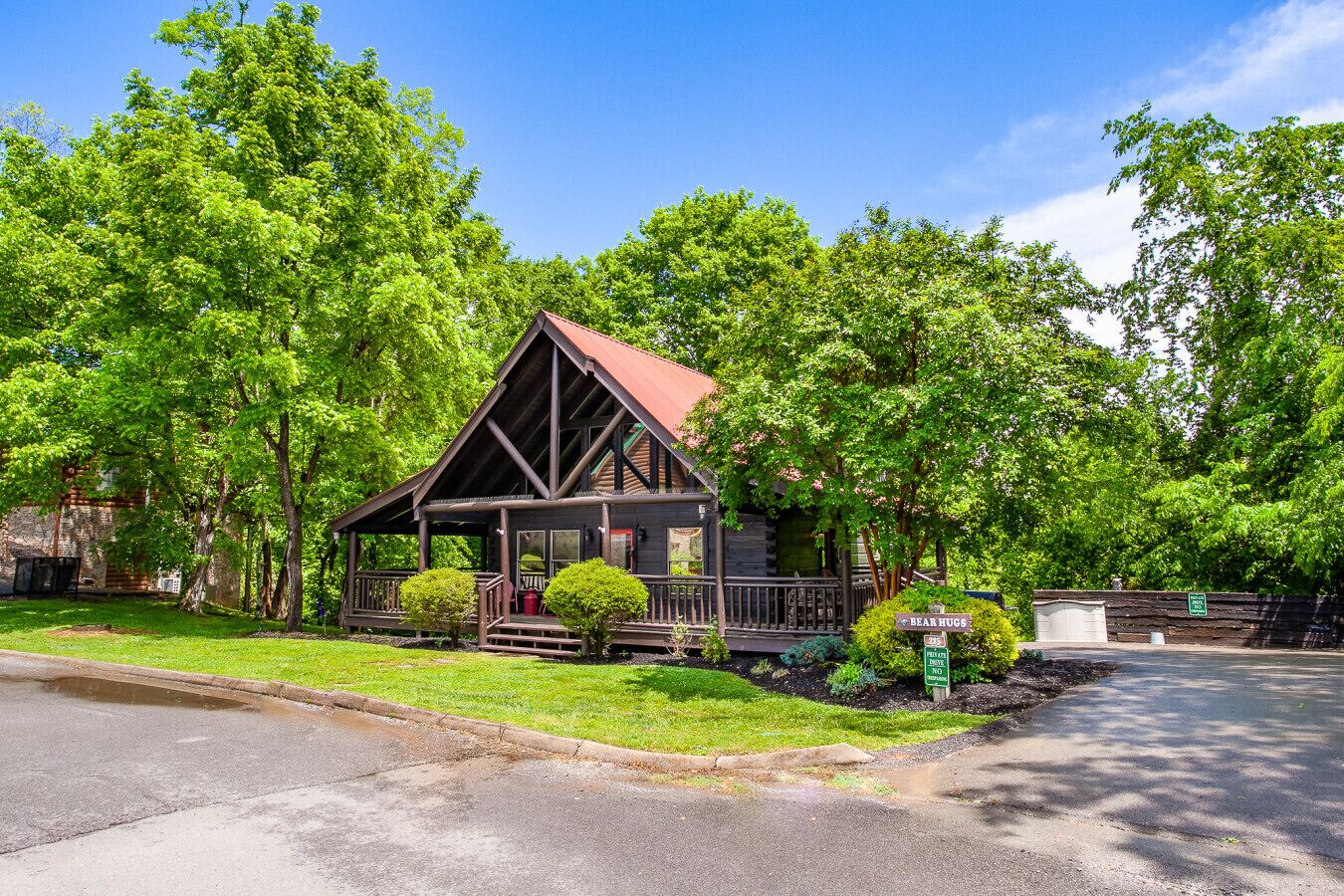 A log cabin with a porch, surrounded by lush green trees.