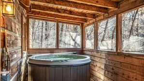 En stuga byggd av trä med ett bubbelbad, stora fönster och utsikt över en skog.