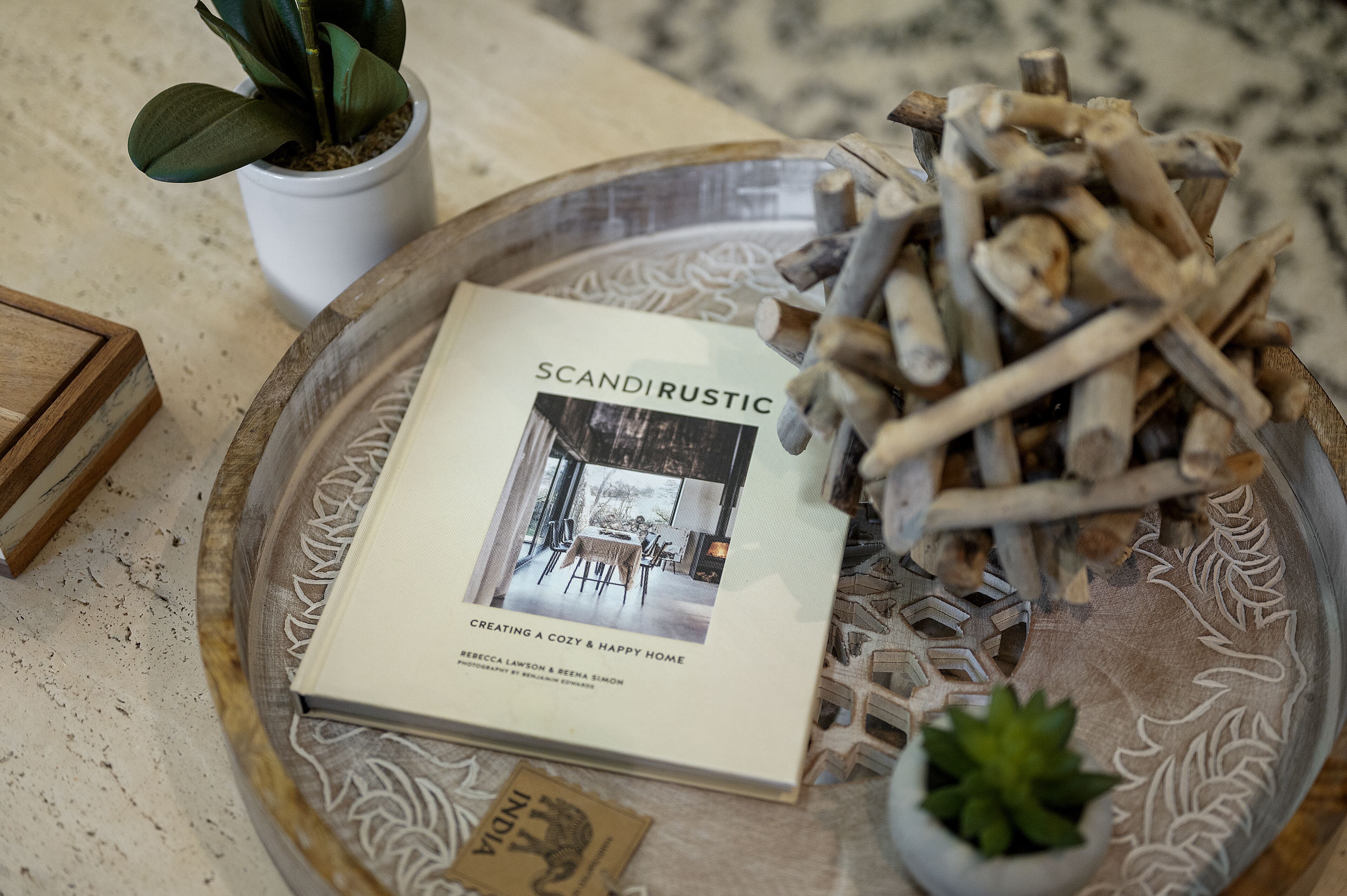 Een boek met de titel 'Scandinavian' op een decoratieve schaal, met een plant en houten stokjes.