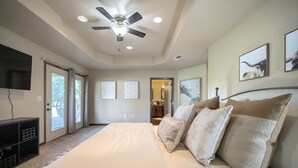 Ein Schlafzimmer mit Bett, Deckenventilator, Kunstwerken und einem Fernseher.