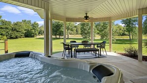 Ein überdachter Patio-Bereich mit Whirlpool, Sitzgelegenheit im Freien und Blick auf eine grüne Landschaft.