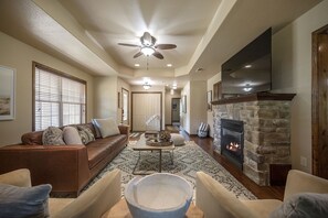 Un salon spacieux doté d’une cheminée, d’un ventilateur de plafond et d’un grand téléviseur.