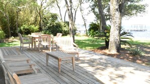 A wooden deck with seating, surrounded by trees and a view of the water. - Modern waterfront home on spacious wooded lot.  Sleeps 6.   (Elberta)