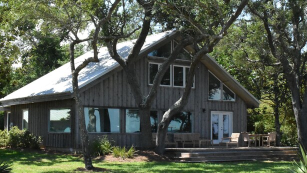 A two-story wooden house with large windows, a covered porch, and a well-maintained lawn. - Modern waterfront home on spacious wooded lot.  Sleeps 6.   (Elberta)