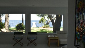 A living room with a view of the sea, two folding chairs, a small table, and a sofa. - Modern waterfront home on spacious wooded lot.  Sleeps 6.   (Elberta)