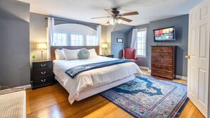 Une chambre à coucher avec un lit, un ventilateur de plafond, une télévision, une commode et une fenêtre.