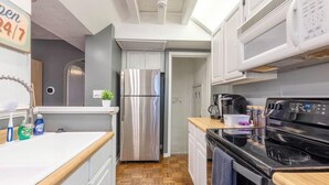 Une cuisine de taille réduite avec des meubles blancs, un réfrigérateur en acier inoxydable, une cuisinière noire et un four à micro-ondes.