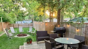 Un jardin avec une terrasse en bois, des meubles en osier, un barbecue et un foyer extérieur.