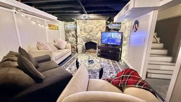 Una sala de estar acogedora con chimenea de piedra, un televisor y una escalera.