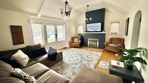 Un salon spacieux avec un haut plafond, une cheminée et un grand téléviseur. On y trouve deux canapés, une table basse et un tapis.