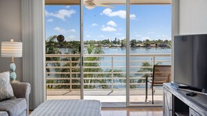 A room with a large sliding glass door leading to a balcony with a view of a body of water and distant buildings.