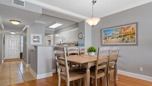 A dining area with a wooden table and chairs, a small potted plant, and a painting on the wall.