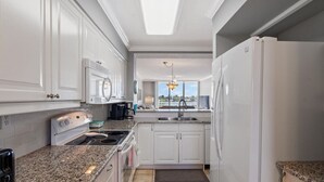 A kitchen with white cabinets, a granite countertop, a stove, a sink, and a refrigerator.