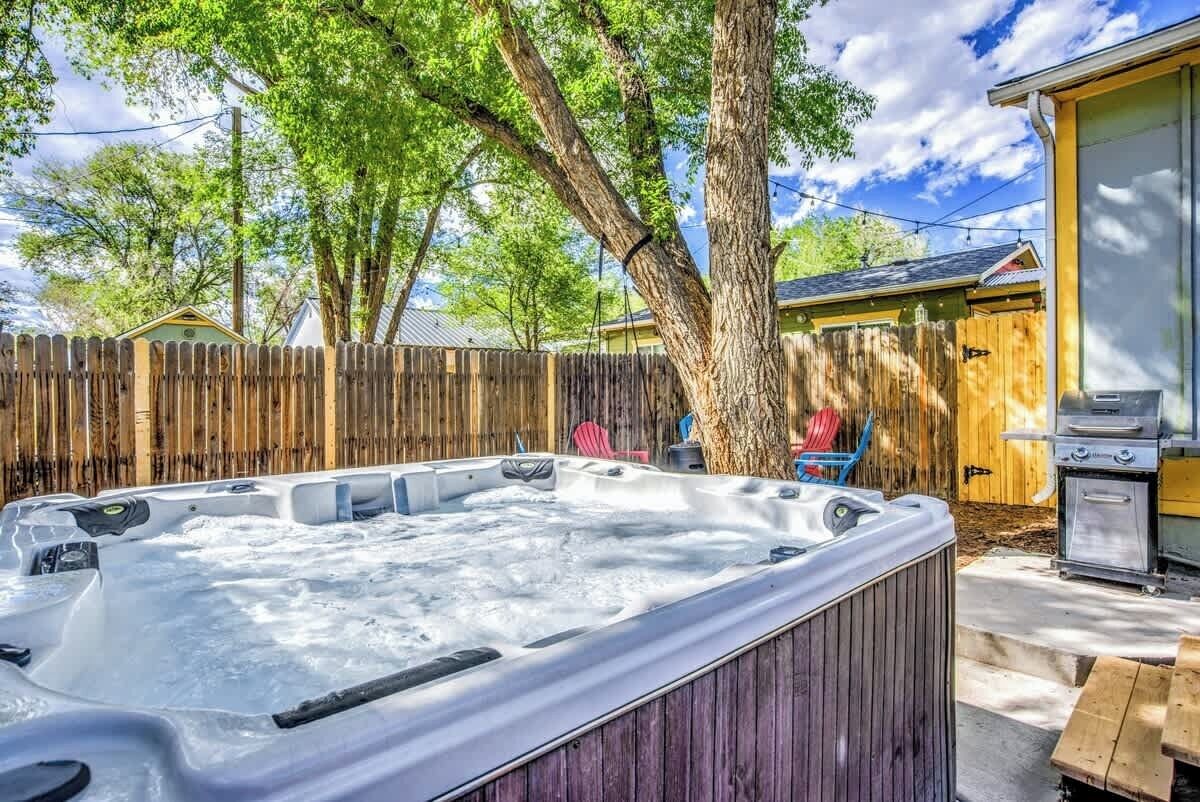 A hot tub in a backyard with a wooden fence, a barbecue grill, and a tree.